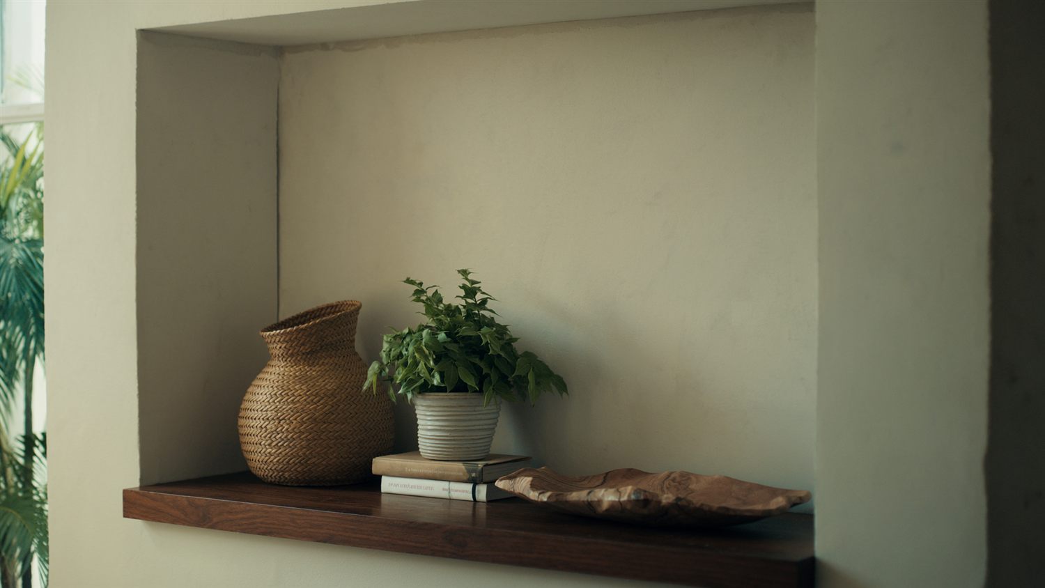 Warm wood shelf decor with a plant, books and a carved tray in an entryway