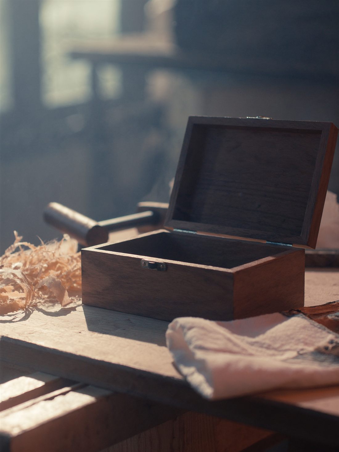 A handcrafted walnut keepsake box being oiled by hand on a workshop bench